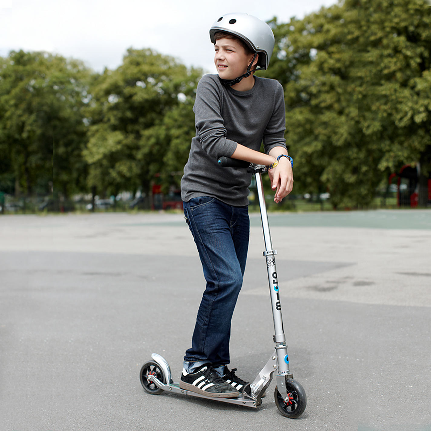 Boy in a helmet standing on a silver Micro Speed+ two-wheel aluminium kick scooter in a park