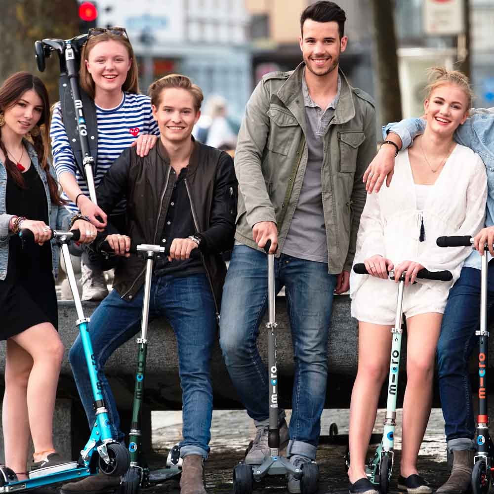 Group of young people posing on the street with several Micro scooters
